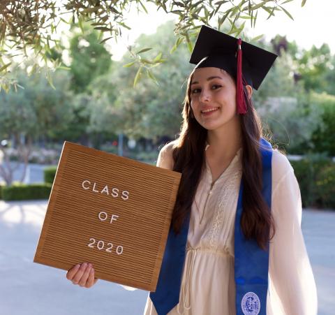Person with a graduation cap holding a sign that reads 